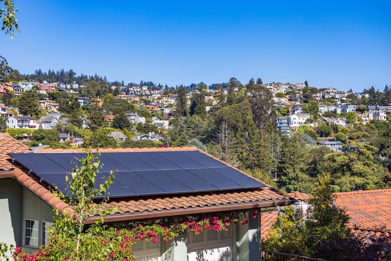 why-choose-us Solar panels on a suburban home, surrounded by lush greenery and a sunny blue sky.