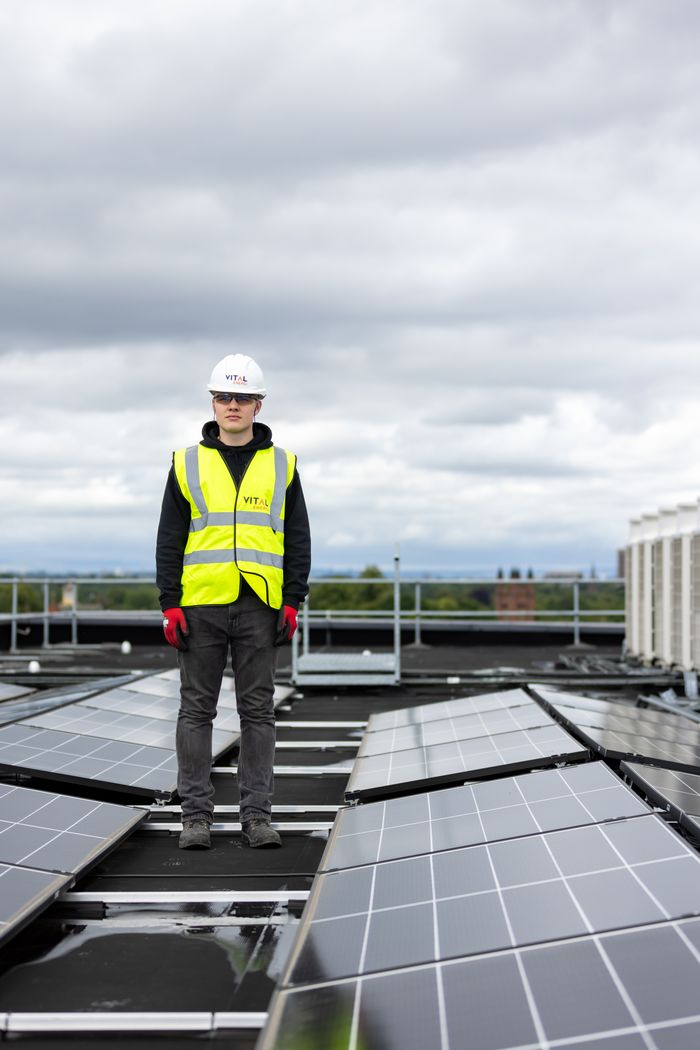 gallery-3 Man in safety vest and helmet inspects rooftop solar panels, promoting renewable energy.